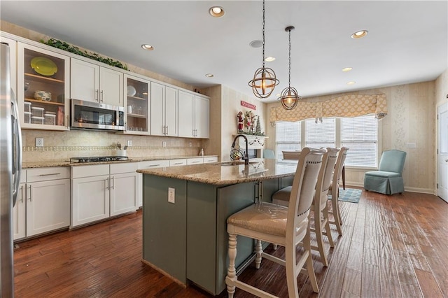 kitchen with light stone counters, white cabinetry, stainless steel appliances, and a kitchen island with sink