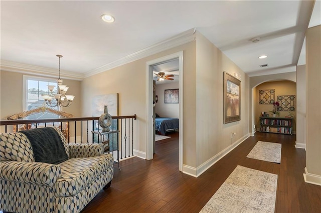 hall with dark wood-type flooring, crown molding, and an inviting chandelier