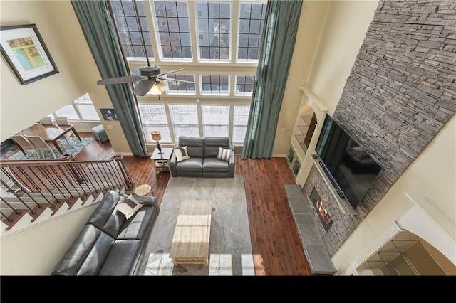 living room featuring ceiling fan, a fireplace, a high ceiling, and hardwood / wood-style floors