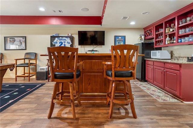 bar with dark hardwood / wood-style floors and black fridge