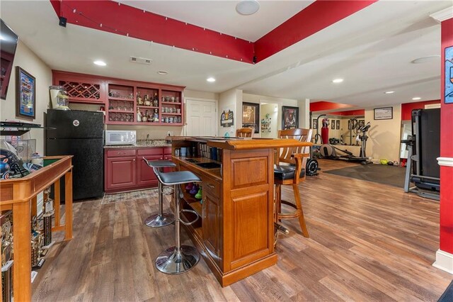 bar with black refrigerator and hardwood / wood-style floors