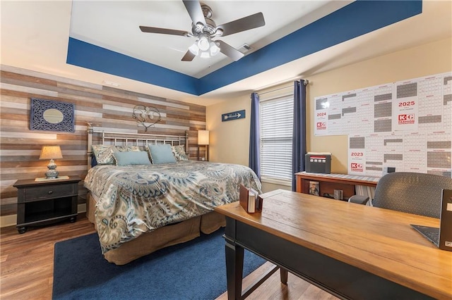 bedroom featuring ceiling fan, hardwood / wood-style floors, wood walls, and a tray ceiling