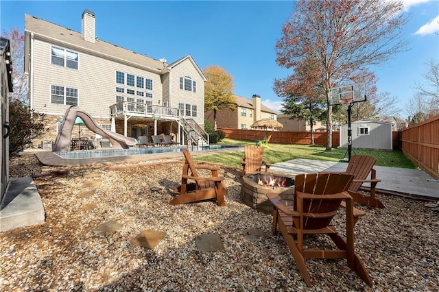 rear view of house featuring a deck, a storage unit, a fire pit, and a patio