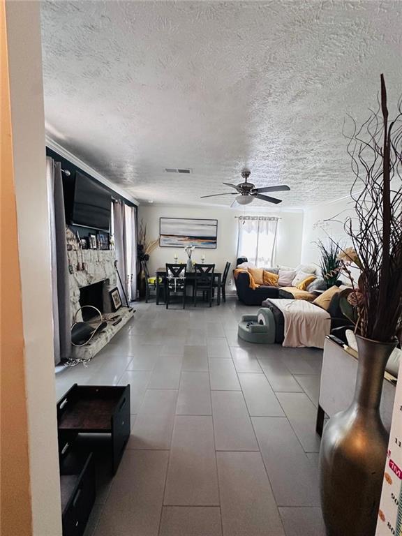 4312 Idlewood Ln, Tucker, GA 30084 - living area featuring ceiling fan, a textured ceiling, a stone fireplace, and tile patterned flooring