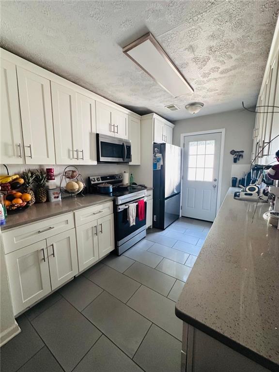 4312 Idlewood Ln, Tucker, GA 30084 - kitchen with stainless steel appliances, a textured ceiling, white cabinetry, light tile patterned flooring, and light stone countertops