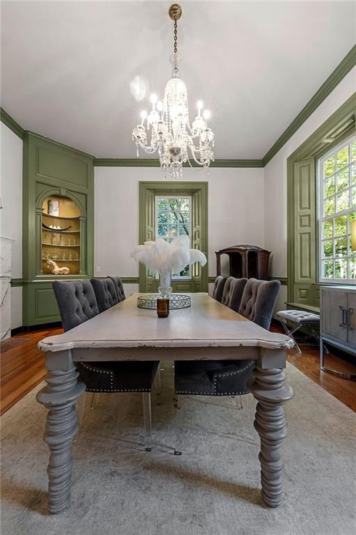 dining area with hardwood / wood-style floors, a healthy amount of sunlight, crown molding, and an inviting chandelier