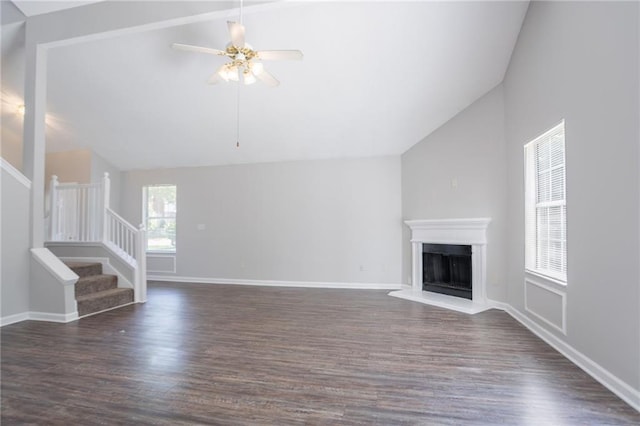 unfurnished living room with vaulted ceiling, stairway, wood finished floors, a ceiling fan, and a fireplace with raised hearth