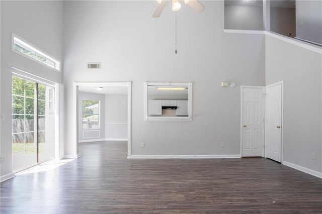 unfurnished living room with a high ceiling, dark wood finished floors, ceiling fan, and baseboards
