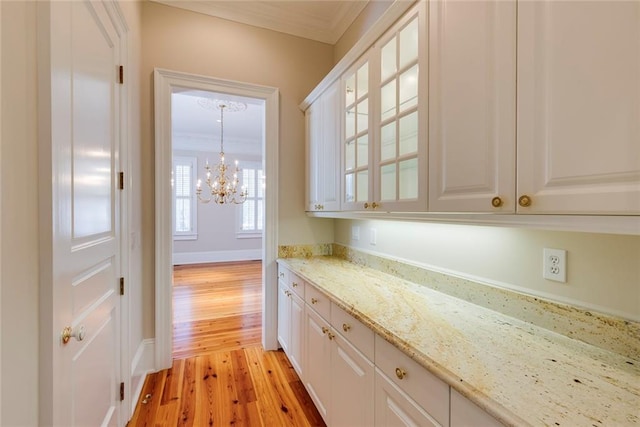 bar with light stone countertops, white cabinets, crown molding, a chandelier, and light hardwood / wood-style flooring