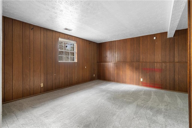 carpeted empty room with wood walls, baseboards, visible vents, and a textured ceiling