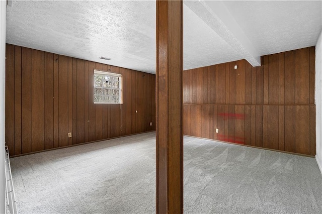 carpeted empty room featuring wooden walls, visible vents, and a textured ceiling