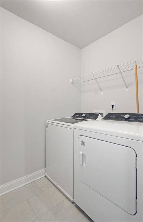 washroom with laundry area, light tile patterned flooring, baseboards, and washing machine and dryer