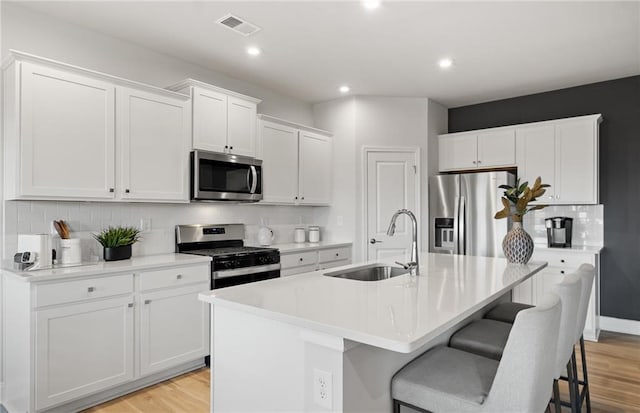 kitchen with a kitchen island with sink, visible vents, a kitchen bar, appliances with stainless steel finishes, and a sink
