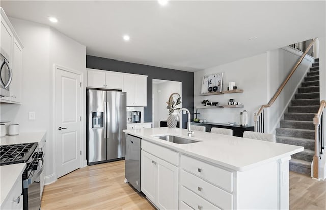 kitchen featuring light wood-type flooring, light countertops, a center island with sink, stainless steel appliances, and a sink
