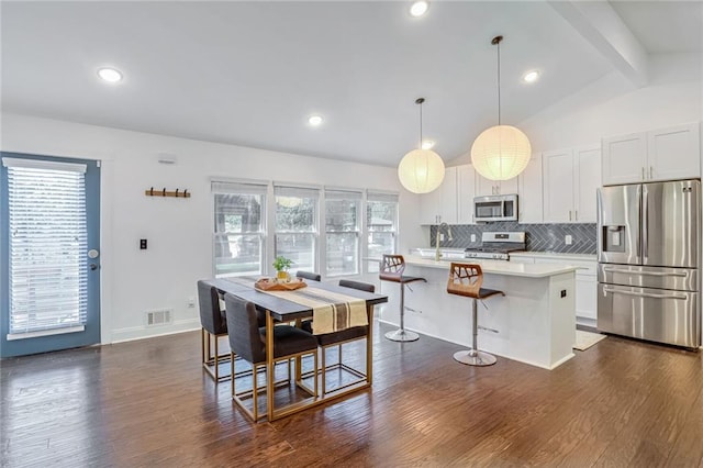 kitchen featuring a kitchen island, lofted ceiling with beams, pendant lighting, white cabinetry, and appliances with stainless steel finishes