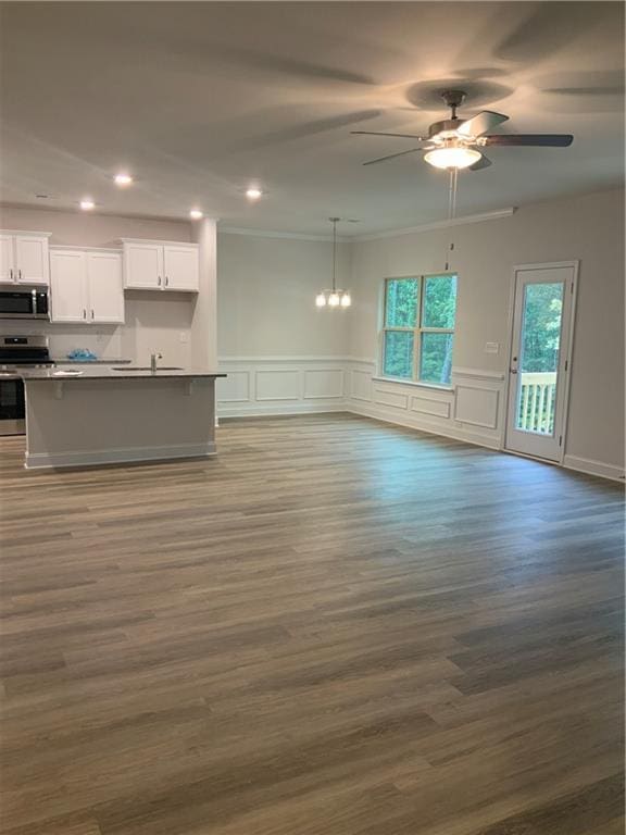 unfurnished living room featuring ceiling fan with notable chandelier, wood-type flooring, and ornamental molding