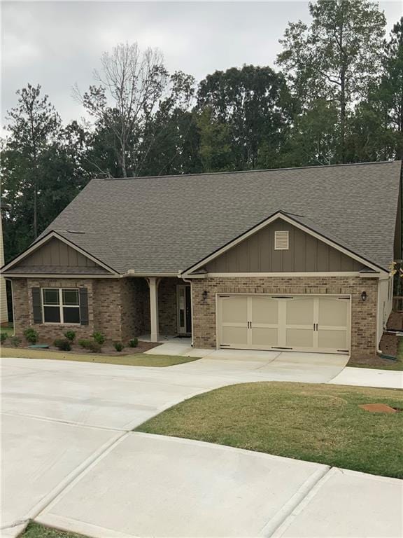 view of front of house with a garage, brick siding, a shingled roof, driveway, and board and batten siding