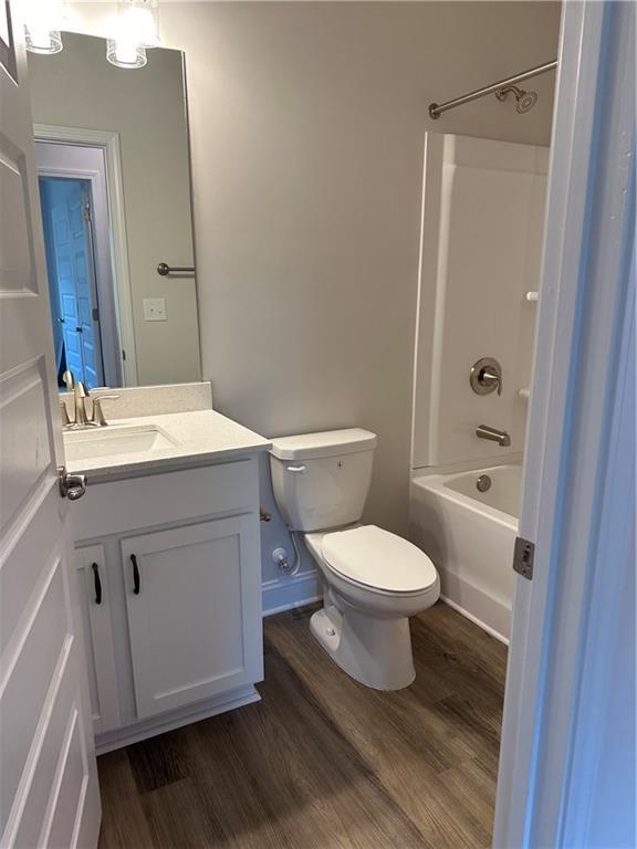 full bath with toilet, bathing tub / shower combination, wood finished floors, and vanity