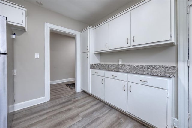 kitchen with white cabinets, stainless steel fridge, light stone counters, and light hardwood / wood-style flooring