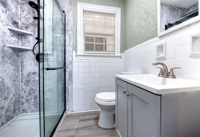 bathroom with vanity, hardwood / wood-style flooring, tile walls, toilet, and a shower with shower door