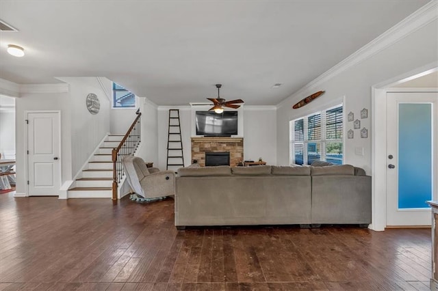 living room with ornamental molding, a stone fireplace, dark wood-type flooring, and ceiling fan