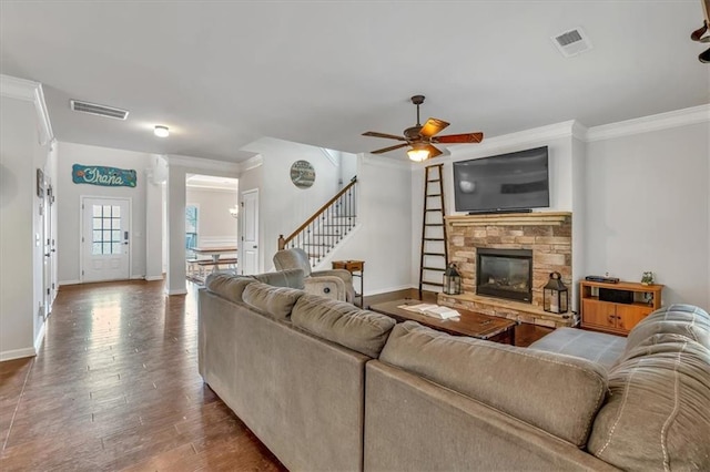 living room featuring wood-type flooring, a stone fireplace, ornamental molding, and ceiling fan