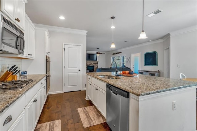 kitchen featuring sink, appliances with stainless steel finishes, light stone countertops, white cabinets, and a center island with sink