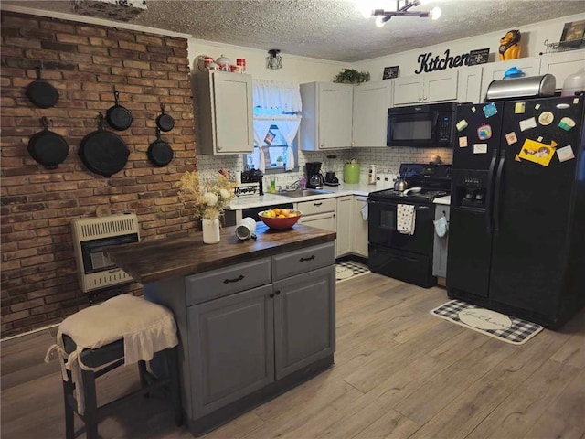 kitchen featuring a textured ceiling, heating unit, sink, black appliances, and light hardwood / wood-style floors