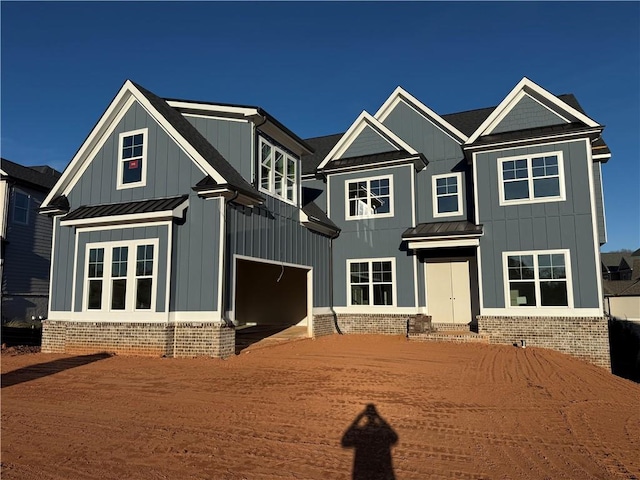 view of front of home with metal roof, an attached garage, dirt driveway, board and batten siding, and a standing seam roof