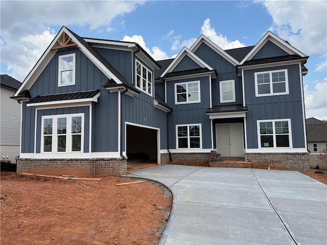 view of front facade with brick siding, board and batten siding, concrete driveway, an attached garage, and a standing seam roof