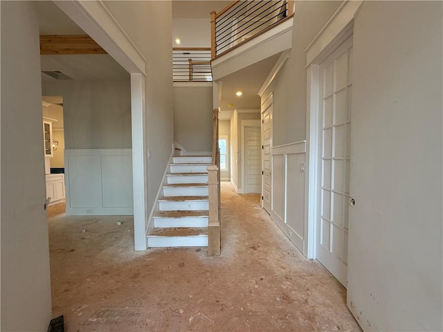 corridor featuring a wainscoted wall, a towering ceiling, stairs, and a decorative wall