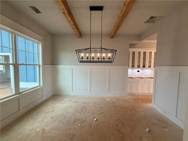 unfurnished dining area featuring wainscoting, beam ceiling, and a decorative wall