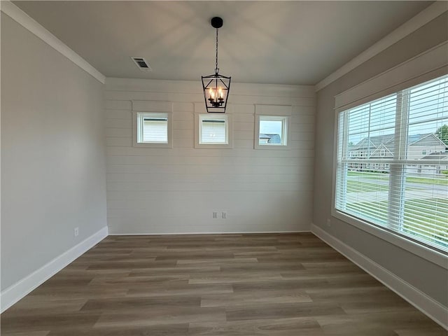 unfurnished dining area with a chandelier, baseboards, wood finished floors, and crown molding