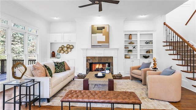 living room with ceiling fan, ornamental molding, a fireplace, and light hardwood / wood-style flooring