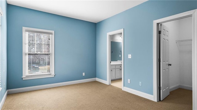 unfurnished bedroom with a walk in closet, ensuite bath, light colored carpet, and a closet