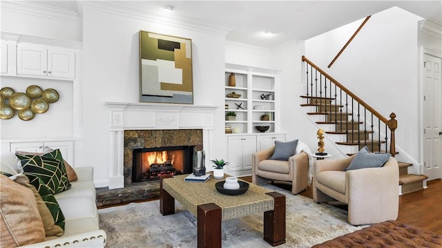 sitting room featuring a tiled fireplace, built in features, wood-type flooring, and ornamental molding