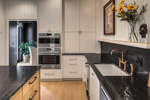 kitchen featuring sink, light hardwood / wood-style flooring, double oven, and dark stone counters