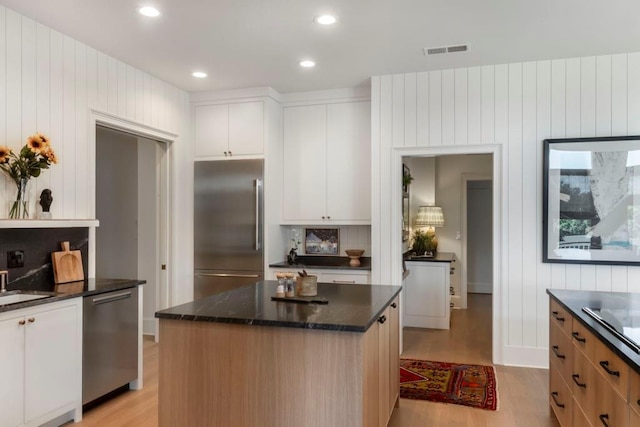 kitchen with light hardwood / wood-style flooring, dark stone counters, a kitchen island, stainless steel appliances, and white cabinets