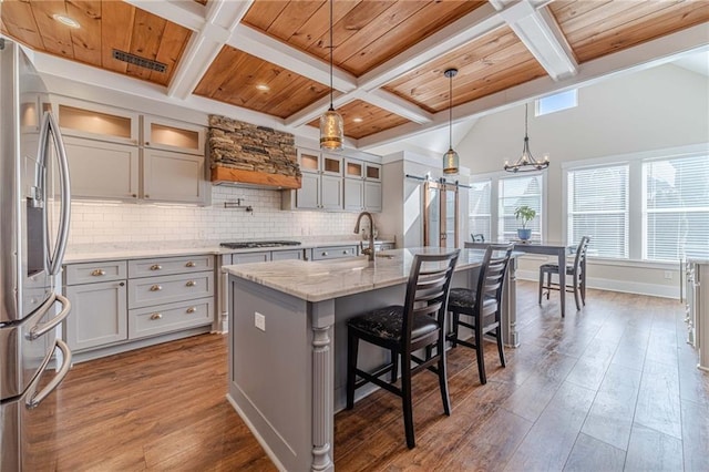 kitchen with appliances with stainless steel finishes, decorative backsplash, hanging light fixtures, a kitchen island with sink, and light stone countertops