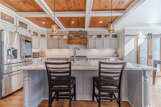 kitchen with hanging light fixtures, coffered ceiling, light stone counters, stainless steel refrigerator with ice dispenser, and a spacious island