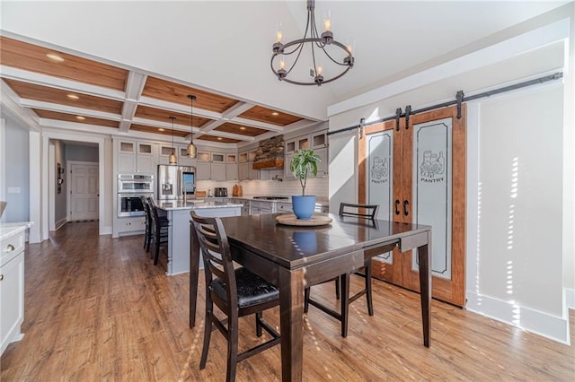 dining space featuring coffered ceiling, beam ceiling, a notable chandelier, a barn door, and light hardwood / wood-style floors