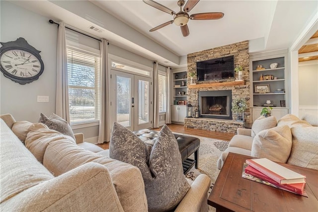 living room with french doors, wood-type flooring, built in features, ceiling fan, and a fireplace