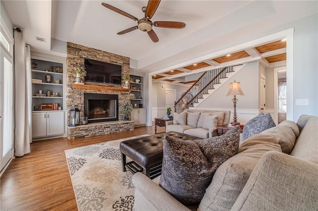 living room featuring beamed ceiling, coffered ceiling, built in shelves, and light hardwood / wood-style flooring