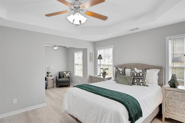 bedroom featuring a raised ceiling, multiple windows, and light wood-type flooring