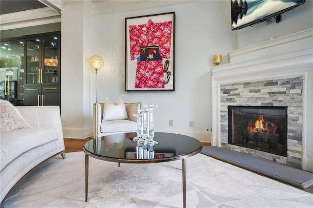 living area featuring a stone fireplace, baseboards, crown molding, and wood finished floors