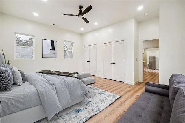 bedroom featuring hardwood / wood-style flooring, two closets, stainless steel fridge, and ceiling fan