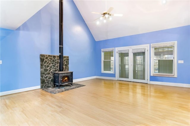 unfurnished living room featuring a wood stove, ceiling fan, high vaulted ceiling, and light wood-type flooring