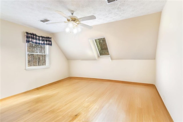 bonus room with lofted ceiling with skylight, ceiling fan, wood-type flooring, and a textured ceiling