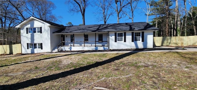 view of front of house featuring a porch, a front yard, brick siding, and fence