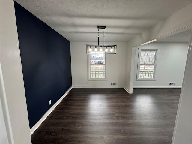 unfurnished dining area featuring baseboards, a textured ceiling, visible vents, and dark wood-type flooring